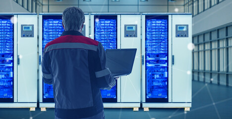 Technician with laptop inspects modern server cabinets in data center. Activity: Information Technology, Data Center Management, Network Infrastructure, Server Maintenance.