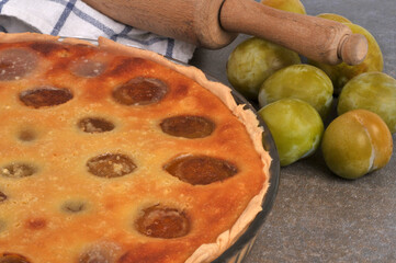 Tarte aux prunes faite maison dans un plat en gros plan avec des prunes entières et un rouleau à pâtisserie