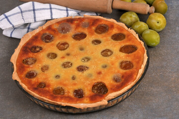 Tarte aux prunes faite maison dans un plat avec des prunes entières et un rouleau à pâtisserie