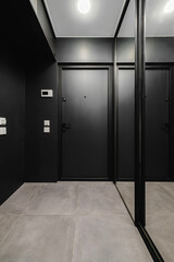 Modern entrance hallway with sleek black decor and large mirror reflecting the door