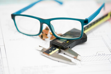 Measuring tools and reading glasses are placed on engineering plans at a workspace for precise...