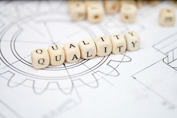Quality message displayed with wooden blocks on a blueprint background in a workspace setting