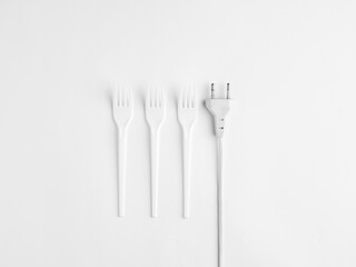 A minimalist still life featuring white plastic forks and an electric plug on a white background, symbolizing modern consumption, artificial living, and energy dependency.