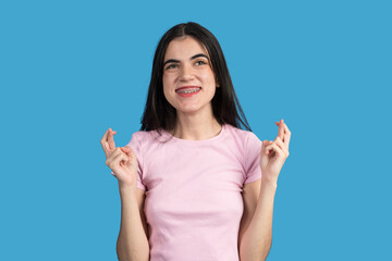 Young woman crossing fingers hoping for good luck on blue background