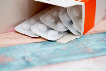 Medication blister pack opened on a wooden surface with colorful background during daylight hours
