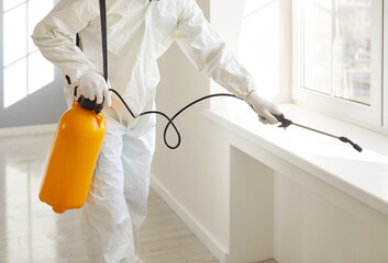 Man exterminator fighting against insects in house spraying poison from sprayer bottle. Worker in...