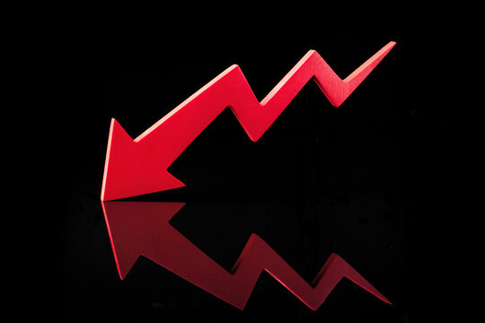 A red zigzag arrow with a downward trend reflects on a black surface, symbolizing financial decline. High quality photo.
