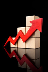 A red upward zigzag arrow next to stacked wooden cubes on a black background with reflection. . High quality photo