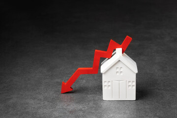 A white house model with a red downward zigzag arrow, symbolizing fall property value, next to keys...