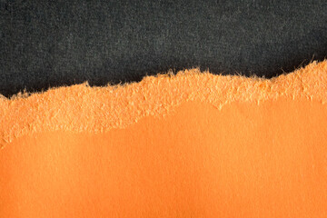 Torn orange paper with rough edges on top of dark gray color paper.