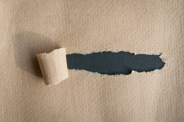 Hole ripped in brown kraft paper on dark gray background.