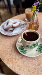 donuts dusted with powdered sugar on a floral plate, served with iced coffee and hot black coffee on a vintage-style café table.