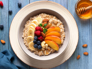 Oatmeal porridge with fresh fruits, honey, and nuts &ndash; natural light, top view