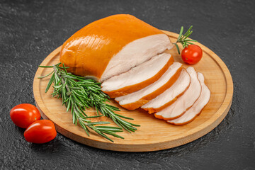 Smoked chicken breast slices on a wooden board with rosemary sprigs and cherry tomatoes