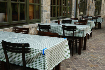 Empty outdoor restaurant terrace in Mokra Gora, Serbia, with green checkered tablecloths and stone walls.