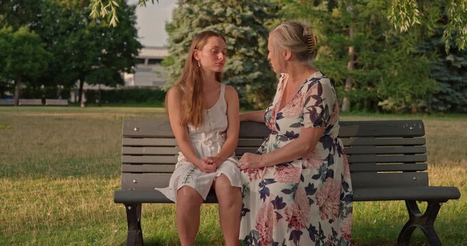 A Young Woman Confides In Her Mother About Her Day. They Sit On A Park Bench And Share A Tender Hug. Dolly Shot To The Right In Warm Natural Light.