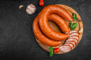 A coiled smoked sausage on a wooden board garnished with garlic, parsley, and cherry tomatoes. top...