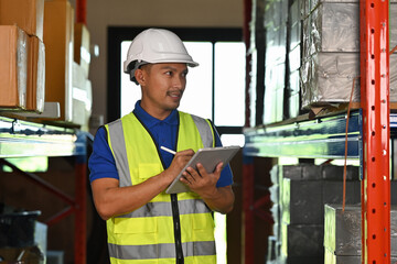 An Asian Man in protective gear managing stock with a tablet in an organized warehouse environment