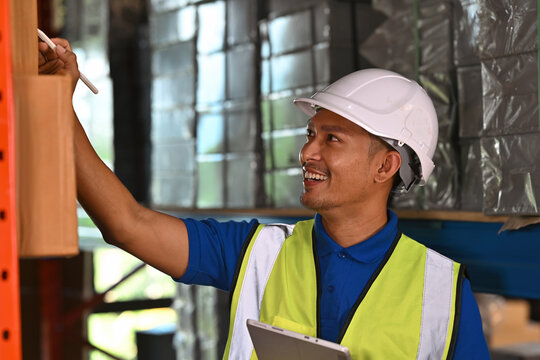 A Logistics worker wearing a hard hat and reflective vest verifies items in the warehouse using modern tools