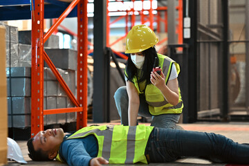 A Female worker in a safety vest calls for help after a colleague collapses on the warehouse floor