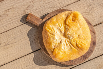 A smoked cheese wheel on a wooden board against a light wood plank background. Top view. Copy space