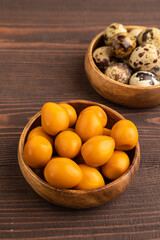 Pile of smoked quail eggs in bowl on a brown wooden. side view.