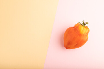 Red heart shape tomato on pink and orange pastel paper, Top view, copy space