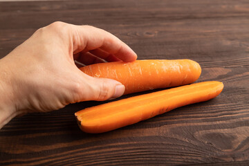 Orange Carrot with hand on brown wooden, Top view, close up