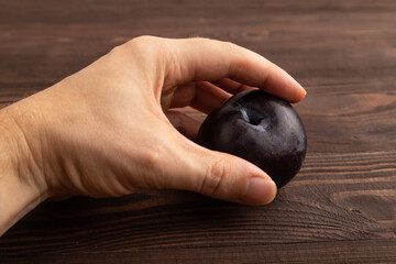 Purple Plum with hand on brown wooden, Side view, close up
