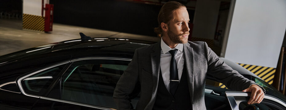 A well-dressed man relaxes beside his stylish car in a modern underground parking space, banner