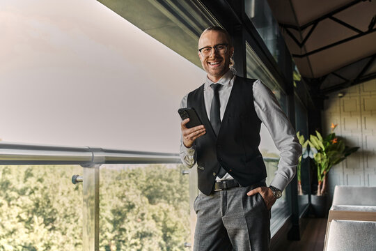 Confident man in stylish suit smiles while using his smartphone in a chic cafe. - Powered by Adobe