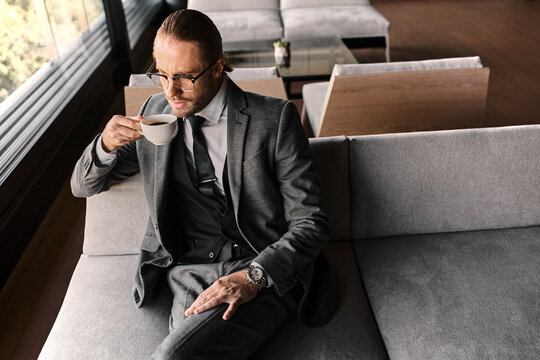 A well-dressed man savors his drink while seated in a stylish cafe, exuding elegance and charm.
