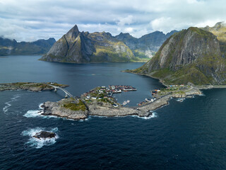Aerial view of jagged peaks meet the tranquil sea, dotted with quaint villages and a bridge connecting islands in Lofoten, Norway.
