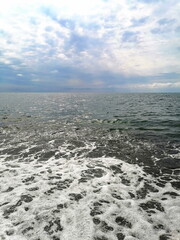 Foamy waves gently wash the shore as the cloudy sky reflects on the sea. A peaceful and refreshing...