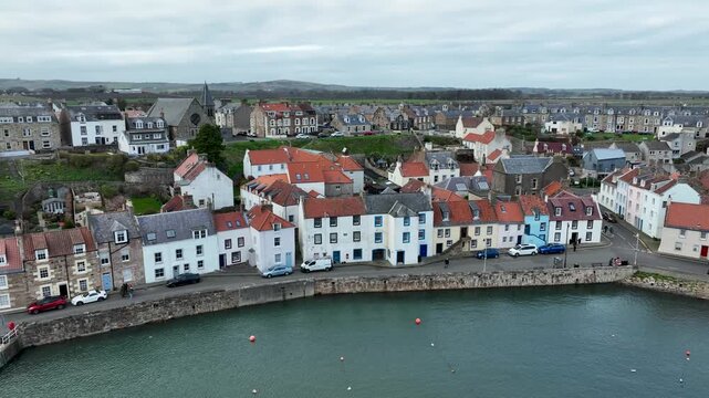 Aerial view of Anstruther showcases a picturesque coastal town with colorful buildings and a serene harbor under a cloudy sky, Anstruther, United Kingdom.