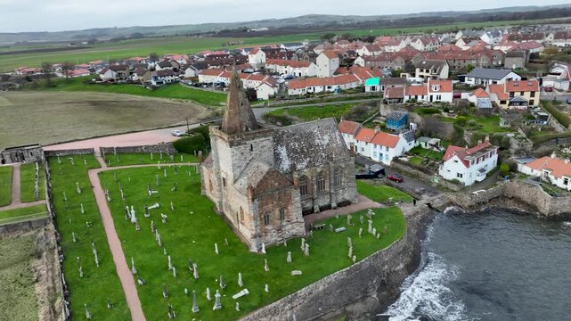 Aerial view of Anstruther Church and graveyard on the coast, with the town's red-roofed houses contrasting with the green fields, Anstruther, United Kingdom.