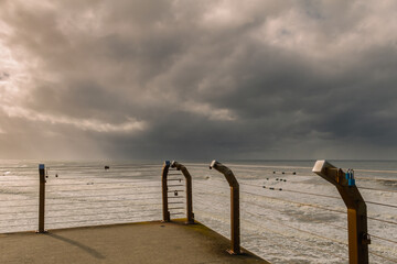 Wild surf and stormy skies form a dramatic backdrop for a stylish backlit fence surrounding a view...