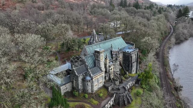 Aerial view of St Conan's Kirk, a historic church with a stunning green roof, surrounded by lush trees and a railway line, Dalmally, United Kingdom.