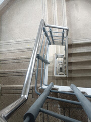 Image shows top down view of staircase with metal handrails and steps made of textured material, creating spiral effect as stairs descend into distance, conveying sense of depth and perspective