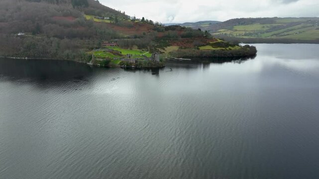 Aerial view of Urquhart Castle ruins, standing majestically on the shores of Loch Ness, with dark water reflecting the sky, Loch Ness, Scotland.