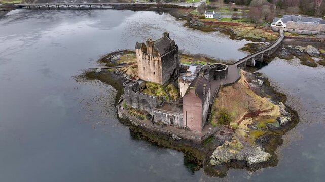 Aerial view of the majestic Eilean Donan Castle sitting on a small island surrounded by dark waters, connected by a bridge, Kyle of Lochalsh, United Kingdom.
