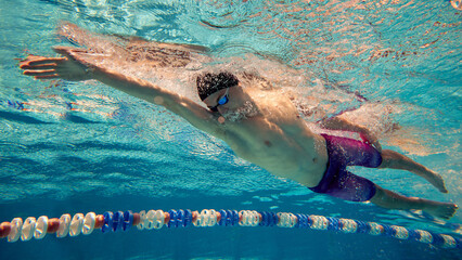 A competitive swimmer practices a freestyle stroke underwater in a pool. Concept of athletic training and sports dedication.