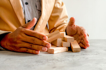 Businessman’s Hands Protect Fallen Wooden Blocks, Symbolizing Crisis Recovery And Risk Control
