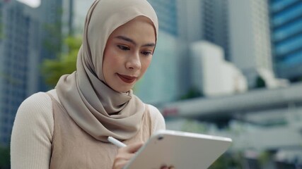 Portrait of woman designer with hijab draws on digital tablet uses stylus in urban environment closeup. Malaysian lady creates graphic artwork with device against office buildings - Powered by Adobe