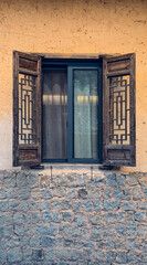Traditional wooden window with intricate geometric lattice design on an earthen wall with natural stone base. Rustic architecture showcasing cultural craftsmanship.