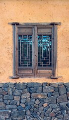 Traditional wooden window with intricate geometric lattice design on an earthen wall with natural stone base. Rustic architecture showcasing cultural craftsmanship.