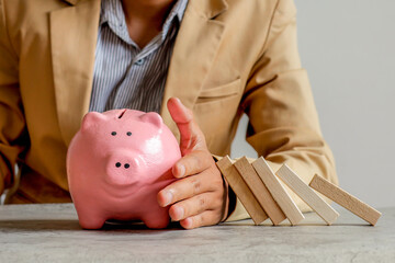Businessman Shielding Pink Piggy Bank From Falling Dominoes