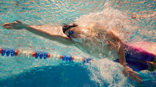 An underwater view captures a swimmer performing the front crawl in a pool. Concept of aquatic sports training and efficiency.