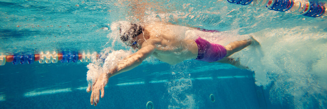 A male swimmer intensely practices his freestyle stroke in an indoor pool, showcasing athletic dedication. Concept of perseverance and athletic training.