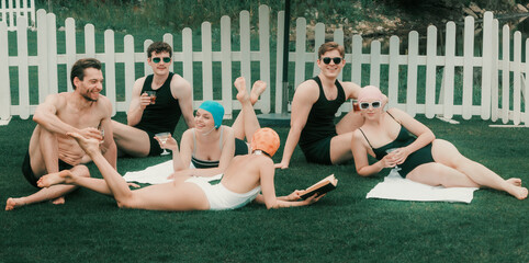 Group of young adults relaxing on grass in vintage swimsuits. Concept of summer joy, retro group...